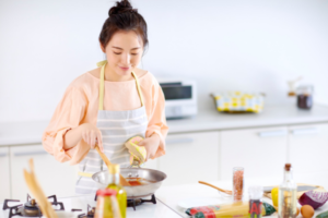 Woman wearing a peach sweater and apron cooks at a bright kitchen stove, squeezing lemon into a skillet.