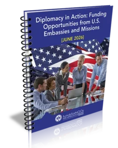 Spiral notebook cover titled 'Diplomacy in Action: Funding Opportunities from U.S. Embassies and Missions [June 2026]' with a diverse team around a laptop in front of a U.S. flag backdrop.