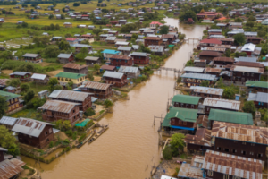 A flooded hillside village with houses on stilts lining muddy water-filled streets.