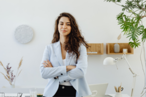 Professional woman with arms crossed standing in a bright, modern office environment.