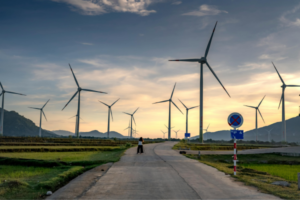 Wind turbines line a rural road at sunset with a person walking in the distance.
