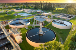 Aerial view of a wastewater treatment facility with circular clarifier tanks and a central control tower at sunset.