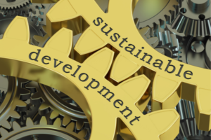 Interlocking gold gears spell out 'sustainable development' against a background of dark metal gears, symbolizing sustainable progress.