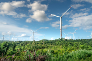 Wind turbines on a green hillside under a blue sky with scattered clouds, part of a wind farm in a lush landscape.