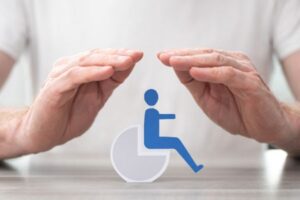 Hands shield a blue wheelchair accessibility symbol, conveying protection and care for people with disabilities.