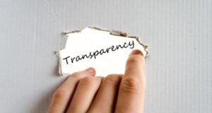 Close-up of torn white paper revealing the word Transparency, held by a finger.